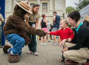 Smokey Bear shaking hands with a child accompanied by his mother.