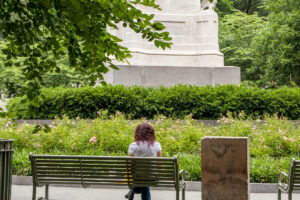 A woman sits on a bench in a green park.