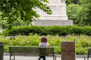 A woman sits on a bench in a green park.